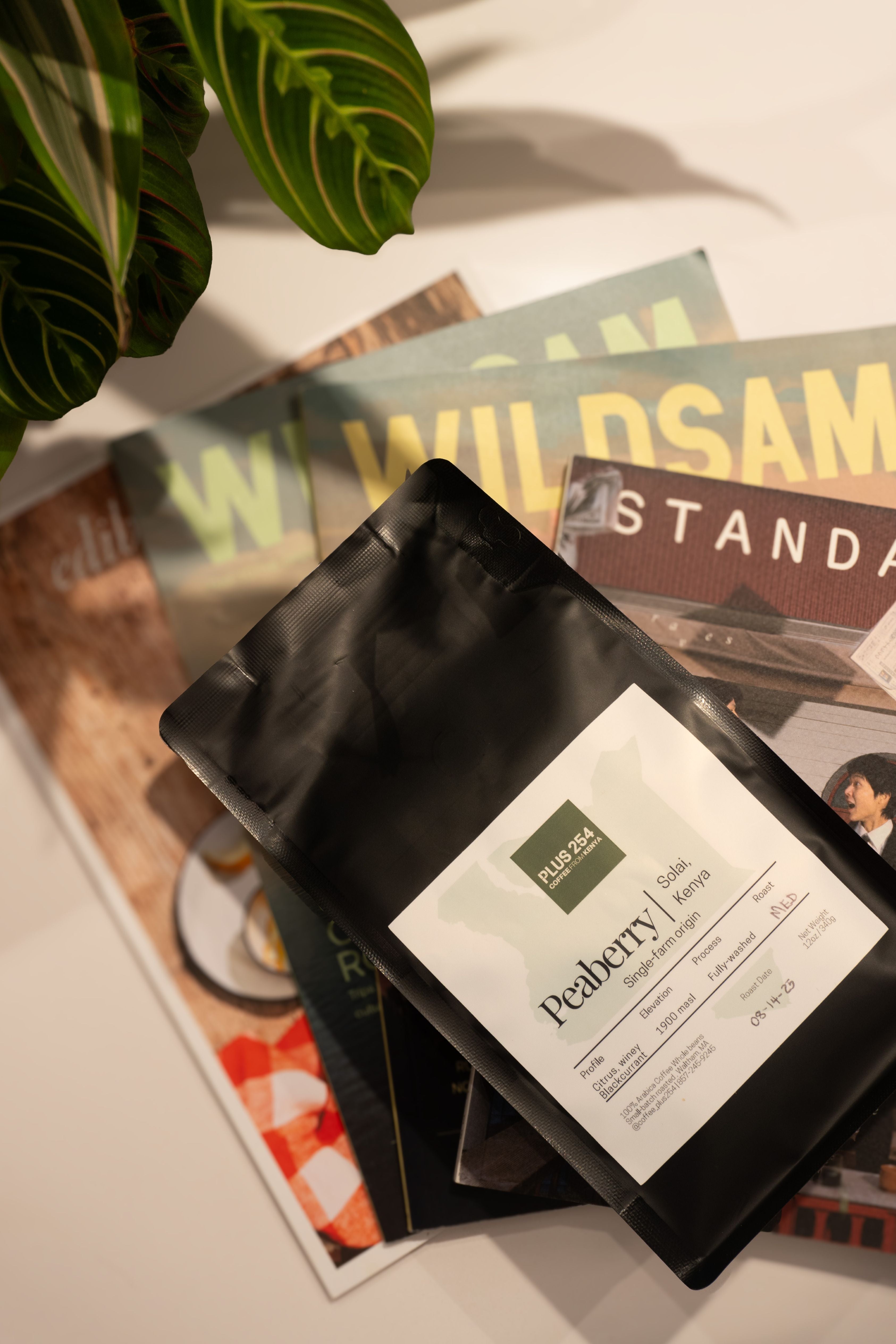 Black coffee bag of Kenyan peaberry coffee with a label on top of magazines